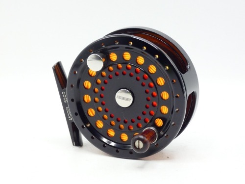A Sage 5300 trout fly reel and spare spool, left hand wind, black anodised model with counter-balanced rosewood handle, block foot, rear spindle mounted milled tension adjuster, only very light use, in original neoprene cases