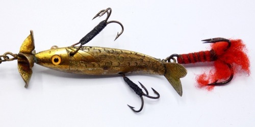 A rare Gregory Acme 3" gilt metal spinning bait, the hollow fish shaped lure with incised scale decoration, slightly curved tail, twin amber and black spot glass eyes, four blade turbine head spinning vanes, hollow spindle shaft with rear treble hook, two
