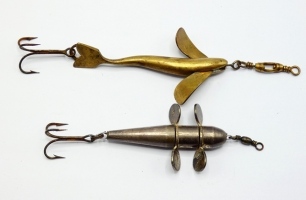 A scarce Pigott style 2 &frac34;" brass bait, the curved fish shaped lure with twin spinning vanes, rear treble hook and box head swivel, circa 1905 and a white metal 2 &frac14;" Devon minnow bait with two twin revolving spinning vanes, rear treble hook and barrel he