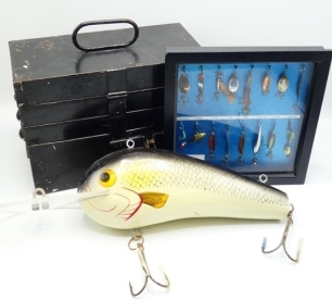 A large wooden shop display plug bait, the 18" long lure with painted decoration, large head vane and twin treble hooks, possibly by Abu, a black japanned cantilevered lure cabinet holding a selection of various Hardy, Pflueger and other baits and mounts,