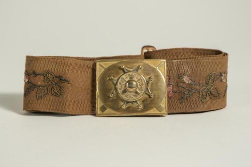 Cricket belt. Early and complete material belt with oblong shaped brass belt buckle showing an eight pointed circle with circle to centre holding a cricket ball and crossed cricket bats, bats and bat handles to corners of the buckle. The buckle measures a