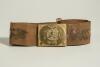 Cricket belt. Early and complete material belt with oblong shaped brass belt buckle showing an eight pointed circle with circle to centre holding a cricket ball and crossed cricket bats, bats and bat handles to corners of the buckle. The buckle measures a