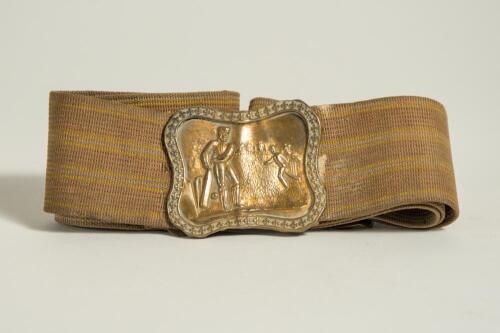 Cricket belt. Early and complete material belt with oblong shaped brass belt buckle showing a bowler bowling to a batsman with trees to background. The buckle measures approximately 2.25&rdquo;x2&rdquo;, the belt in brown material with minor stripes running through i