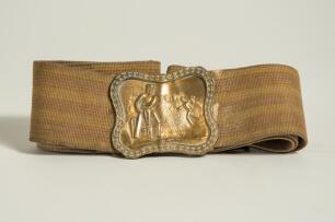 Cricket belt. Early and complete material belt with oblong shaped brass belt buckle showing a bowler bowling to a batsman with trees to background. The buckle measures approximately 2.25&rdquo;x2&rdquo;, the belt in brown material with minor stripes running through i