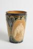 Doulton Lambeth stoneware beaker, moulded with relief vignettes of cricketers, a batsman, bowler and wicket keeper, Abel, Woods and McGregor in white on a brown background. With stylised daisy and floral leaf Art Nouveau decoration to top and sides in gre