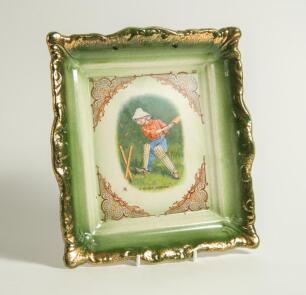 Edward Patrick Kinsella. A rectangular ceramic wall plaque, after Kinsella, printed with a portrait of a boy cricketer wearing the distinctive white floppy hat, with stumps and bails flying having played his shot. Title to lower half &lsquo;A Missed Boundary&rsquo;. 