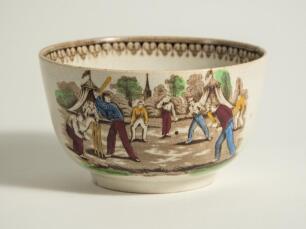 Village cricket bowl. Staffordshire 19th century mug, transfer printed in black with two scenes of village cricket, with church and tents to background, floral and oak leaf inner rim decoration. Hand coloured in green, burgundy, blue and yellow. Approx 5.