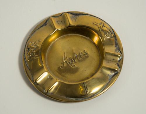 &lsquo;Ashes&rsquo;. Brass ashtray with title impressed to centre, to side rims images of a kangaroo with bat under his arm and lion tossing a ball into the air and to lower rim a set of three stumps and cricket ball. 3.75&rdquo; diameter. Some wear otherwise in good condi
