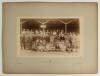 W.G. Grace early 1900s. Large early original sepia photograph of an athletics presentation ceremony taking place in front of a grandstand, dignitaries standing at a table of trophies with Grace third from the right, young athletes seated in front, and onl