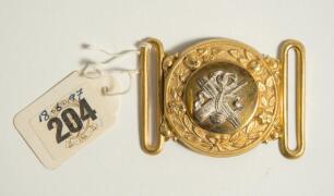 Cricket belt buckle. A circular shaped belt buckle in soft gilt metal, made as a tradesman&rsquo;s sample, of circular form with rose border in relief and with applied silver plated design of bat, bound stumps and ball at centre. Ball decoration to corners of b