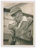 Arthur Edward Robert Gilligan. Cambridge University, Surrey, Sussex & England 1919-1932. Mono photograph of Gilligan, half length, wearing M.C.C. blazer and England cap lighting up his pipe. Signed in ink to the photograph by Gilligan. The photograph meas